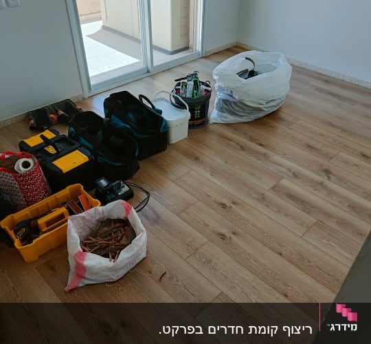 רצפת פרקט עם כלי עבודה ושקיות בחדר